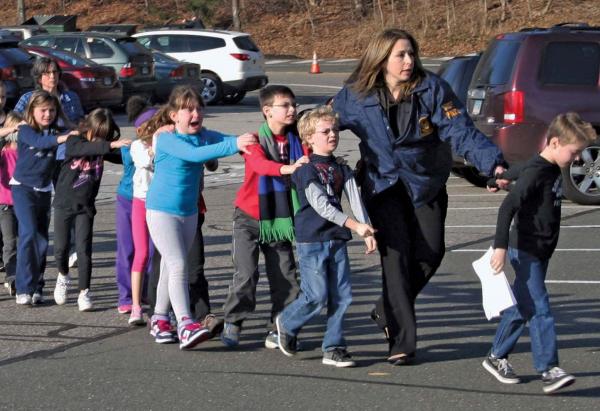 A state police officer leading children out of the Sandy Hook Elementary School in Newtown, Connecticut, after a mass shooting at the school on December 14, 2012.