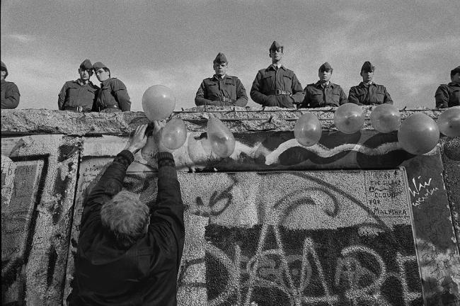 A West German man places balloons on the wall as East German “Vopos,” or Volkspolizei, watch from atop it near the Brandenburg Gate in Berlin, West Germany on Nov. 4, 1989, by James Nachtwey